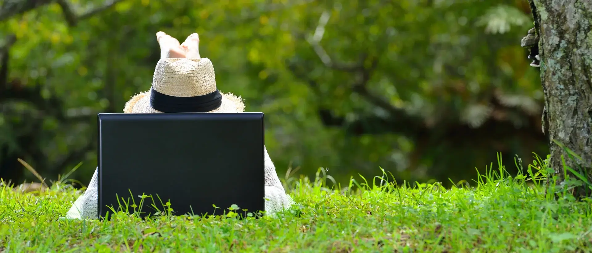 photo d'une personne avec un chapeau couchée sur l'herbe devant un ordinateur