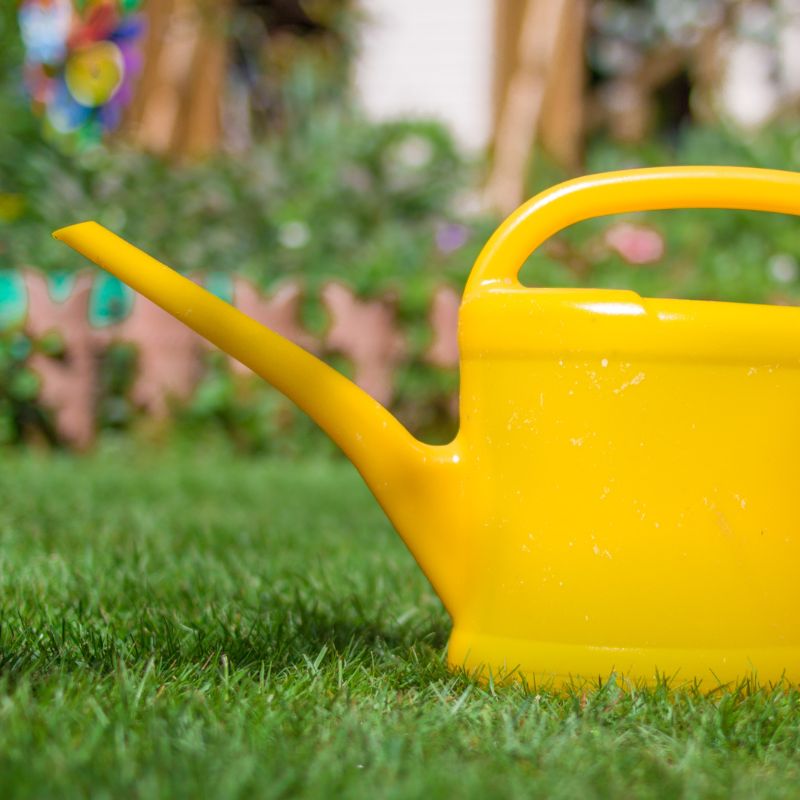 Un arrosoir jaune posé sur la pelouse