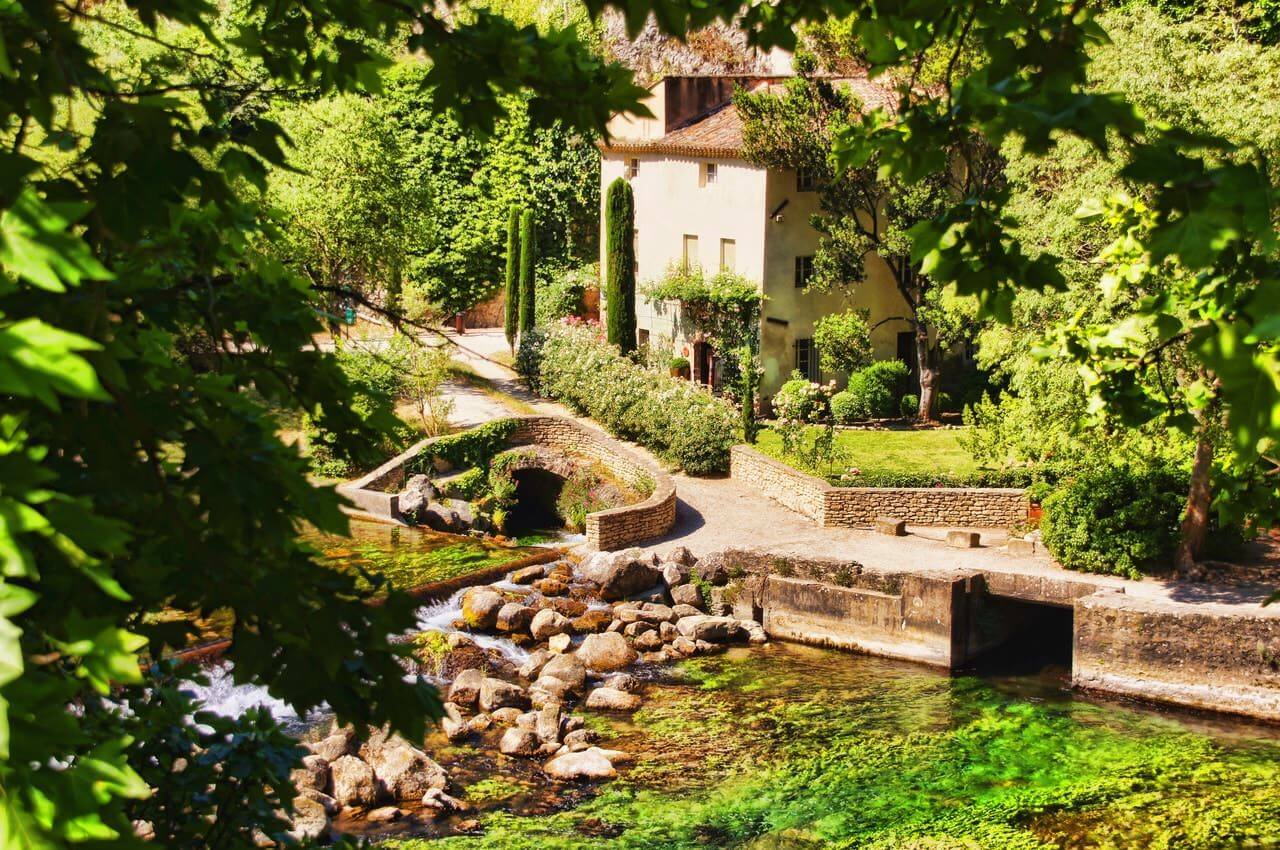 view of a typical southern house with a small stream flowing in front of it and a stone bridge