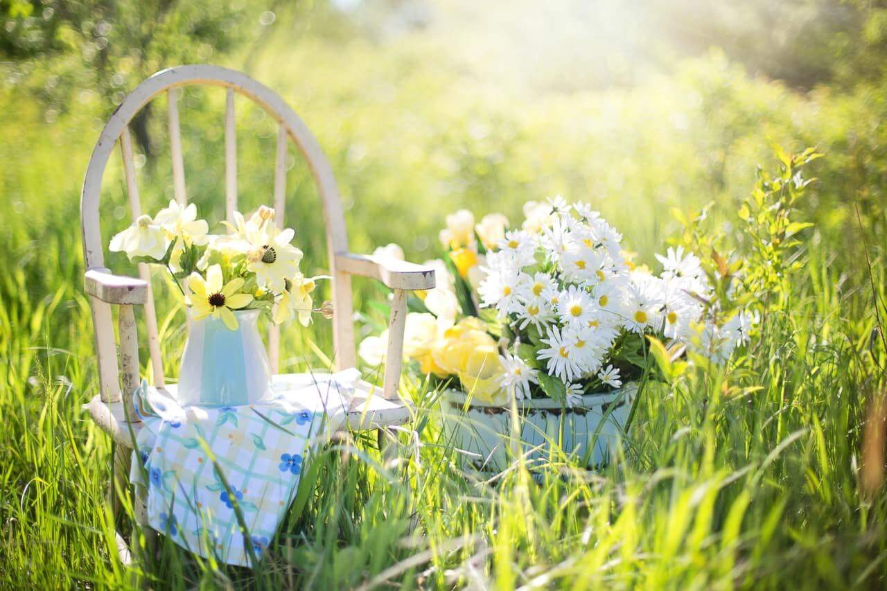small wooden chair with a vase of flowers placed on it next to a basket full of daisies