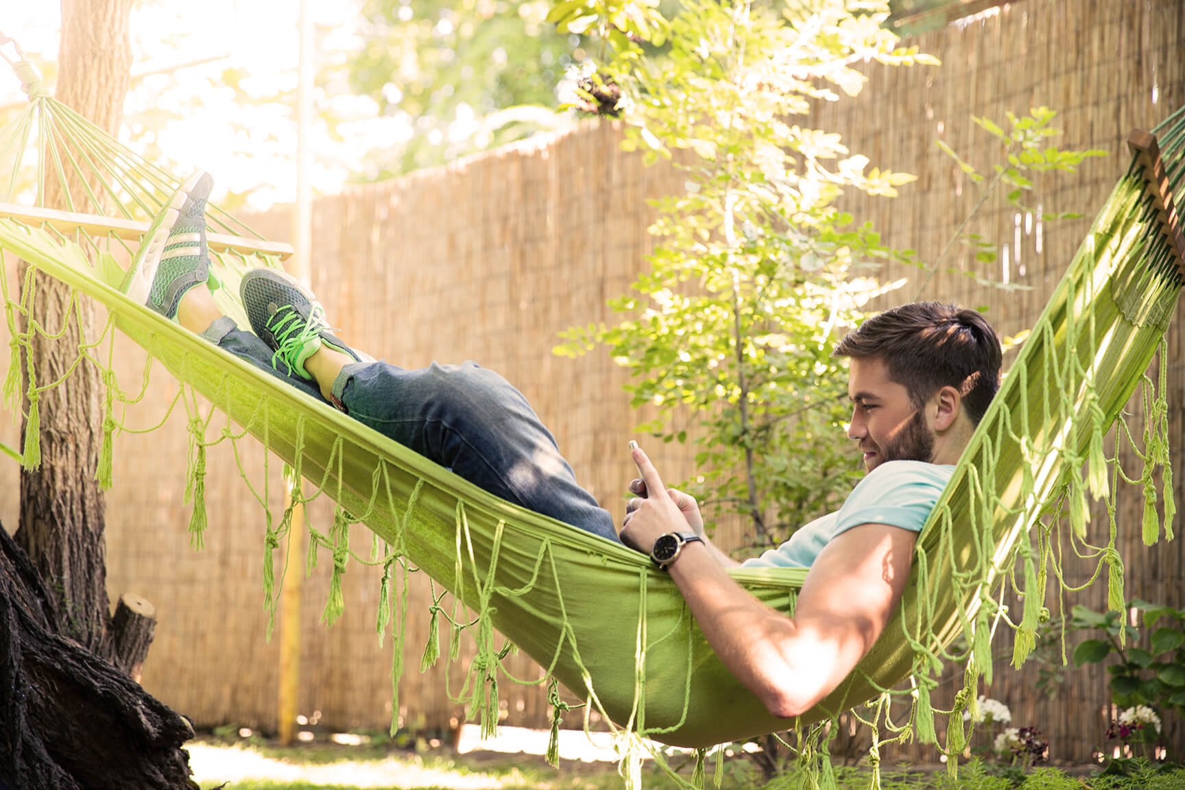 Man looking at his phone lying in a hammock in a garden