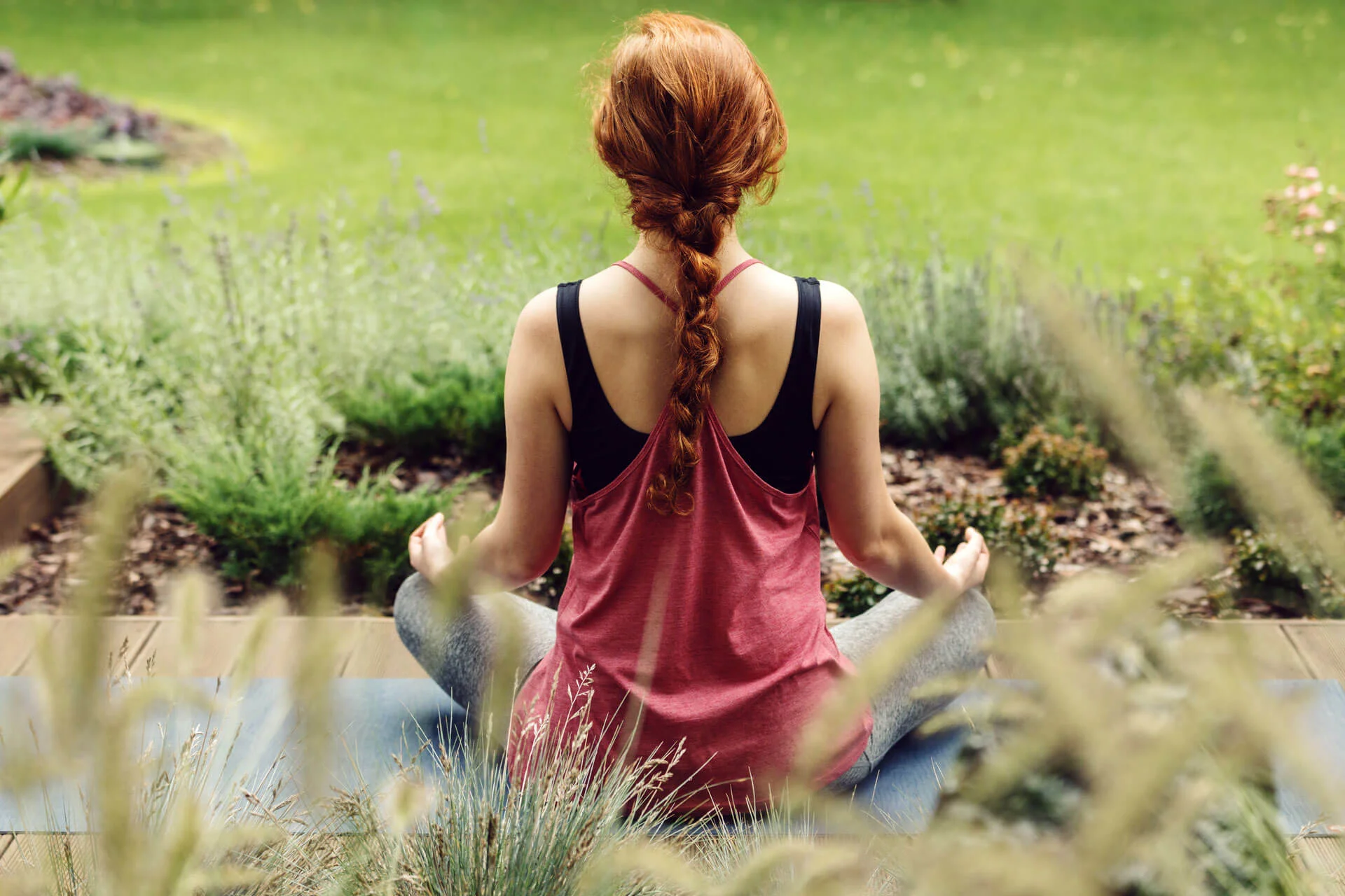 photo d'une femme assise en tailleur en train de méditer sur une terrasse dans un jardin